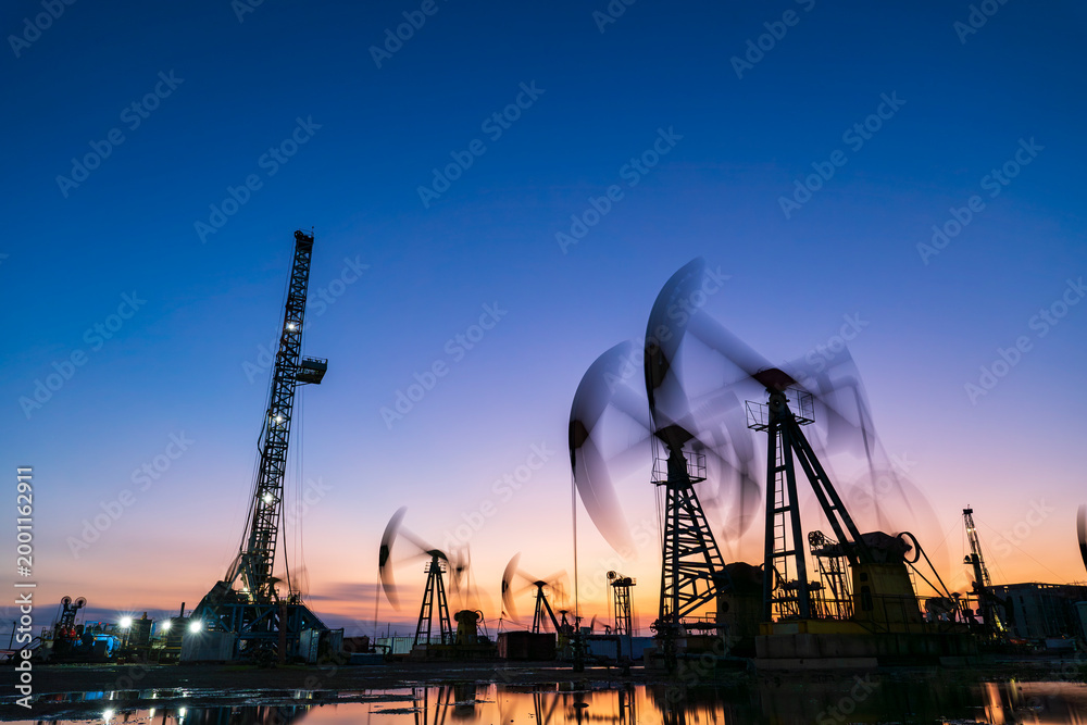 Obraz premium in the evening, oil pumps are running, The oil pump and the beautiful sunset reflected in the water, the silhouette of the beam pumping unit in the evening.