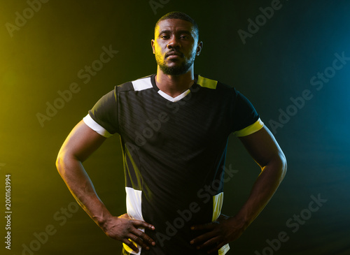 Mid-adult African man posing in studio wearing black white jersey with yellow and cyan rim lights