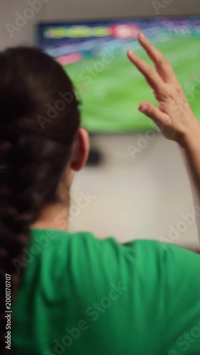 Latin Woman wearing a green shirt cheering for her favorite team while watching a soccer game on television at home, celebrating a goal and showing emotional support