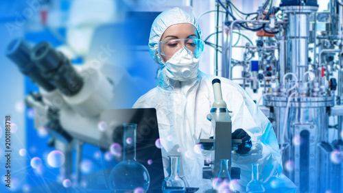 Schilderij op canvas Pharmaceutical manufacturing, researcher in protective suit operates microscope