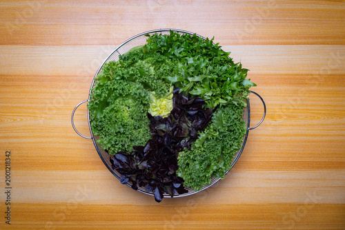Top view of assorted fresh lettuce in metal basket on wooden table, green and red leaves, organic salad ingredients, healthy food concept with copy space for text or image, clean minimal background.