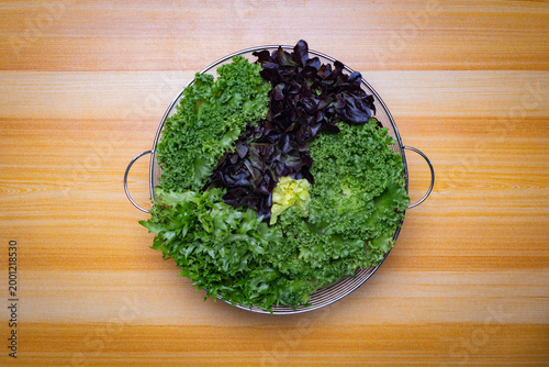 Top view of assorted fresh lettuce in metal basket on wooden table, green and red leaves, organic salad ingredients, healthy food concept with copy space for text or image, clean minimal background.