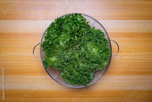 Top view of assorted fresh lettuce in metal basket on wooden table, green and red leaves, organic salad ingredients, healthy food concept with copy space for text or image, clean minimal background.