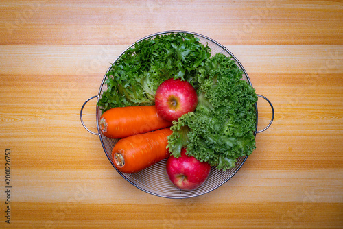 Top view of fresh vegetables and fruits in metal basket on wooden table, green lettuce, red apples and carrots, healthy organic food concept with copy space for text or image, clean minimal background