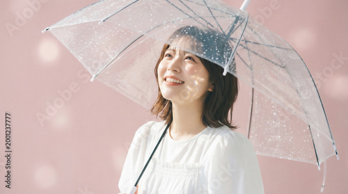 Happy Japanese woman looking up under a clear vinyl umbrella against a pink background