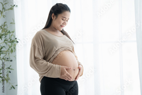 Pregnant asian woman holds hands on belly touching her baby caring about her health Beautiful happy pregnant woman tender mood photo of pregnancy. Free Download Pregnant asian woman holds hands on belly touching her baby caring about her health Beautiful happy pregnant woman tender mood photo of pregnancy. - GFXLoad