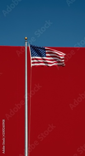 Red background and blue sky with an American flag waving on a tall silver pole for patriotic holiday marketing, national celebration banners and political design