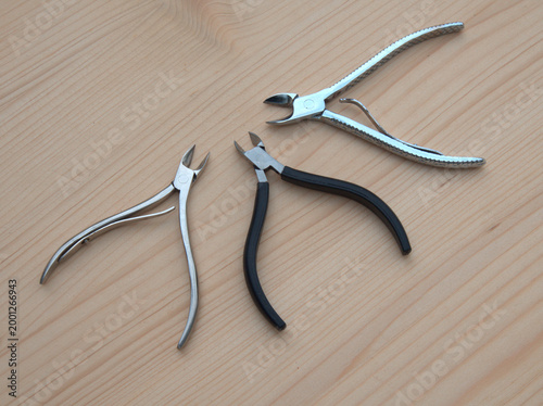Three nail nippers and cuticle cutters placed on a light wooden surface. Close-up top view of professional manicure and pedicure tools made of stainless steel