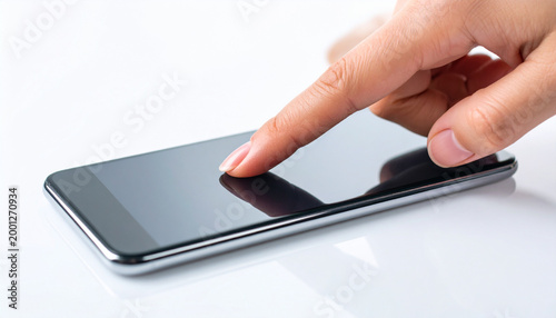 Close-up of a finger touching a smartphone screen on a white reflective surface, highlighting mobile technology interaction.