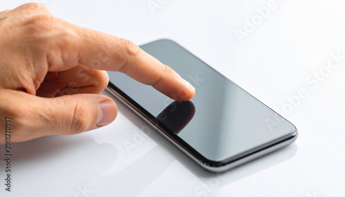 A close-up shot shows a human hand with an index finger poised to interact with the blank, reflective screen of a sleek smartphone on a white surface.