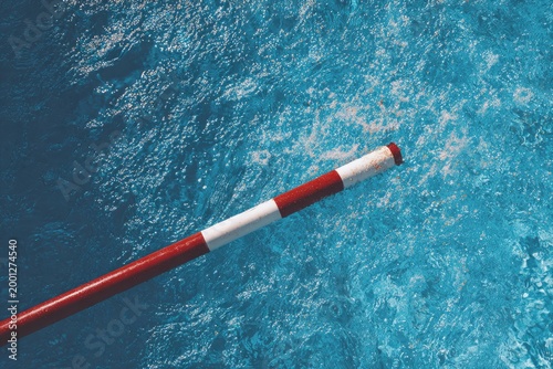 Red and White Pole Extending Over Rippling Blue Water Surface.