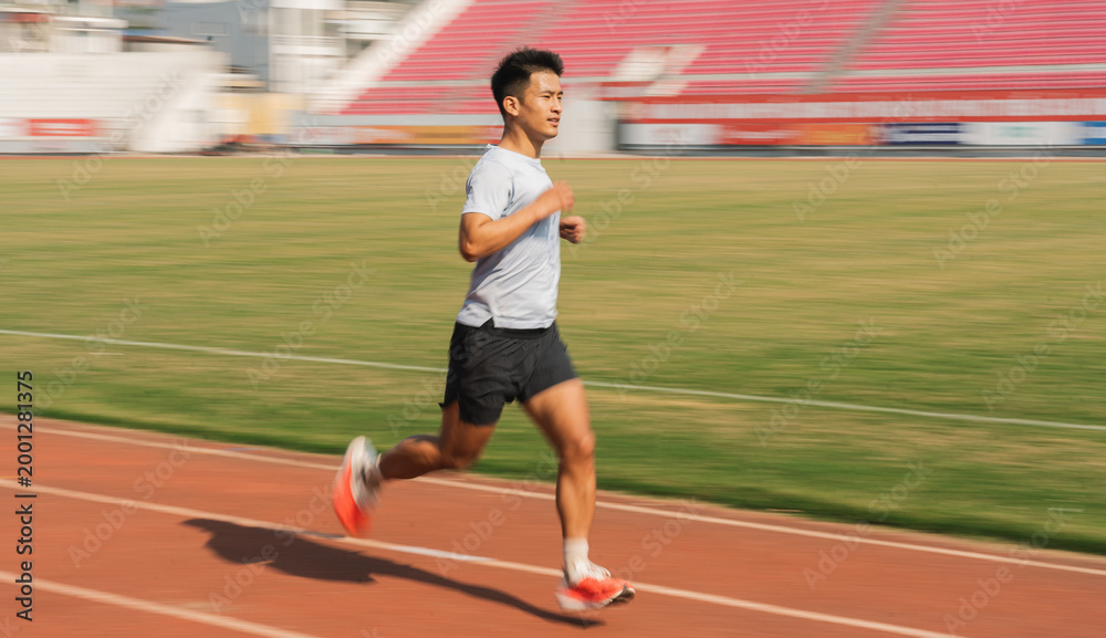 Fototapeta premium A focused athlete sprints on an outdoor track stadium seating blurred in background