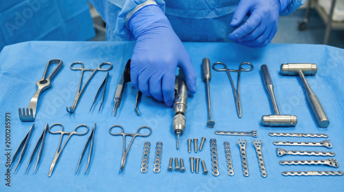 Gloved hands of focused surgeon arranging high precision orthopedic surgery setup. Various surgical instruments and tools ready on sterile blue drape for complex operation