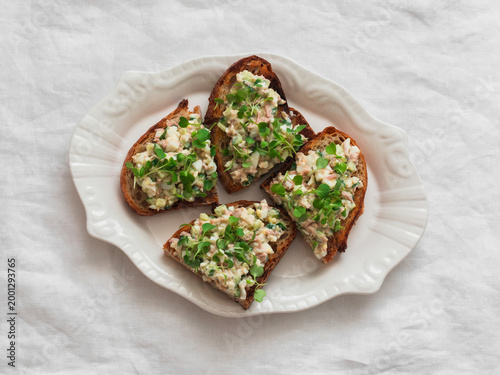 Tartine bread sandwich with canned tuna, eggs, cucumber salad on a light background, top view