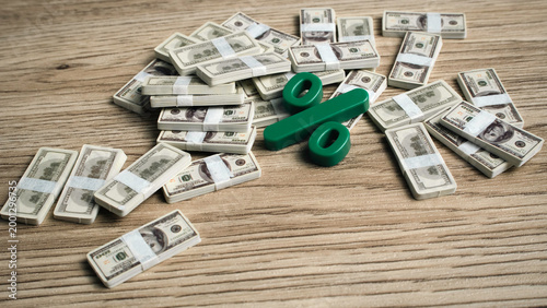 Photos Green percentage symbol surrounded by many stacks of hundred dollar bill bundles on a wooden table