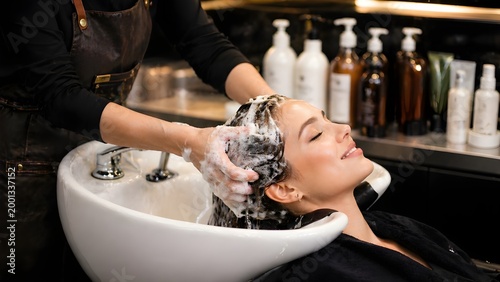 Professional hairstylist washing woman's hair at salon shampoo station