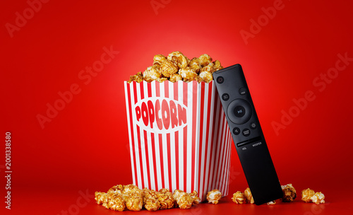 Popcorn and TV remote on red background