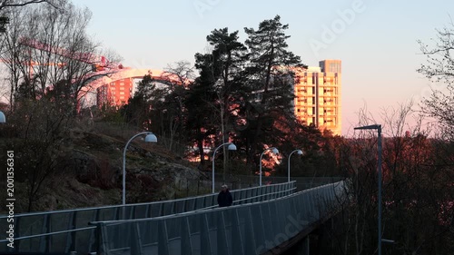 Stockholm, Sweden A man walks on a pedestrian path, Vikdalsvagen, in the Nacka suburb and the Svindersviksbron bridge in the background. 