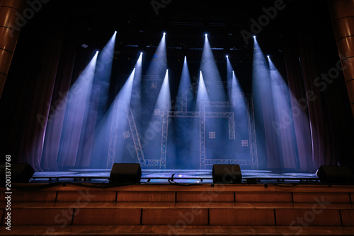 Stage setup with multiple spotlights illuminating a performance area, featuring a wooden floor and backdrop curtains in a theater environment