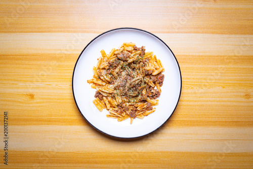 Top view of pasta with minced beef sauce on white plate over wooden table, rich Italian comfort food, savory texture, rustic style, homemade meal, warm tones, restaurant quality cuisine gourmet dining