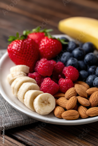 Healthy snack plate with fresh strawberries, blueberries, raspberries, sliced banana, and almonds. Organic fruit and nut platter for nutritious diet.