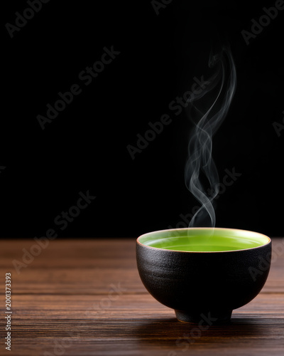 Steaming cup of hot Japanese green tea in a traditional ceramic bowl. Peaceful Zen atmosphere with green liquid and rising steam on black background.