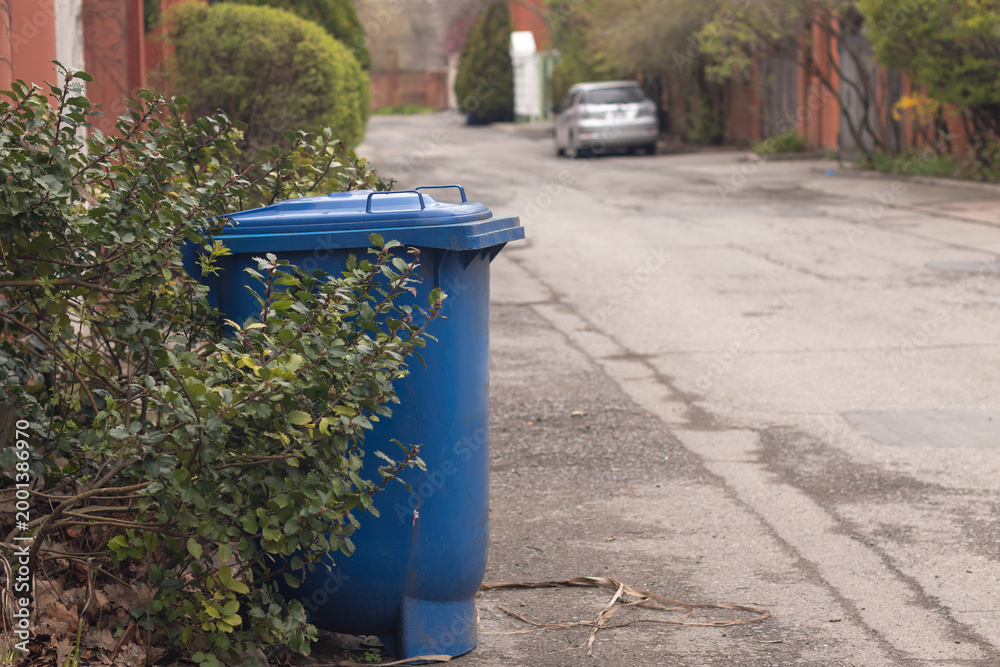 Obraz premium Blue plastic recycling bin for paper waste stands at the roadside in the suburbs