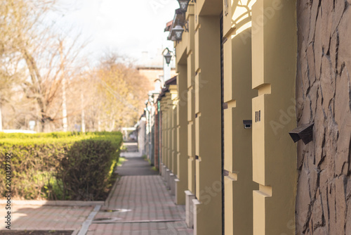 A yellow wall of a suburban house illuminated by sunlight and trimmed bushes in the background