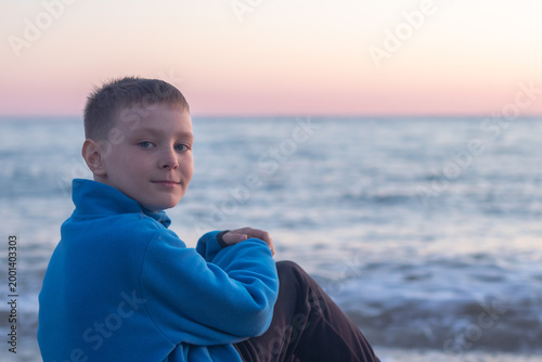 Portrait of a nine-year-old boy in a blue sweatshirt against the backdrop of the sea