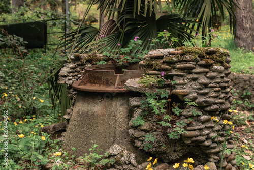 An old concrete manhole with an open hatch without a cover, lined with stonework, located in foliage