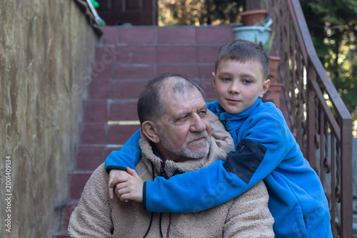 A nine-year-old boy in a blue sweatshirt hugging his grandfather while standing on the porch of his family home.