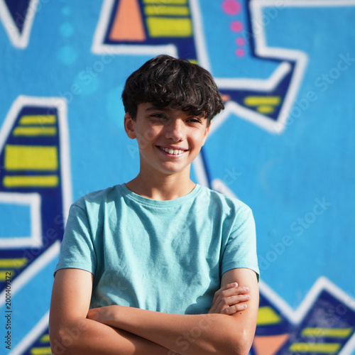 Portrait of preteen boy smiling with arms crossed and wearing blue child t-shirt. colorful defocused background