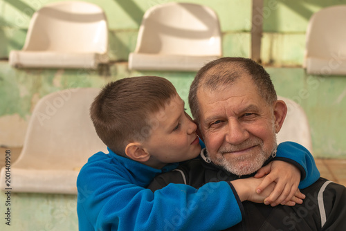 Young  boy embracing grandfather sitting in the empty stands of a sports facility.