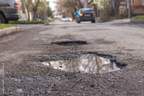 Pothole in the road with a car moving away in the background