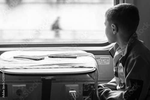 Cute boy sitting on a train and looking out the window. Black and white image
