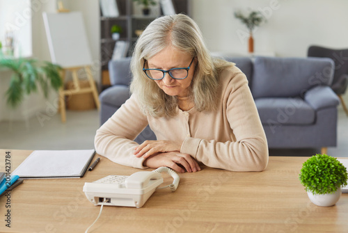 Tableau sur toile Nervous senior woman waiting for phone call near telephone at home, anticipating communication and news, senior tension in a escape zone filled with anxious expectation and concern