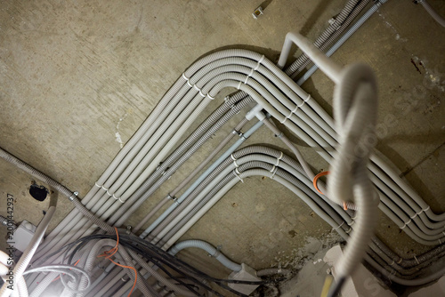 Damaged electrical cables hanging from concrete ceiling in building. Building renovation area featuring unsafe wiring and inadequate safety measures during construction