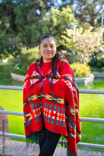 Peruvian indigenous woman wearing traditional poncho standing outdoors by green pond