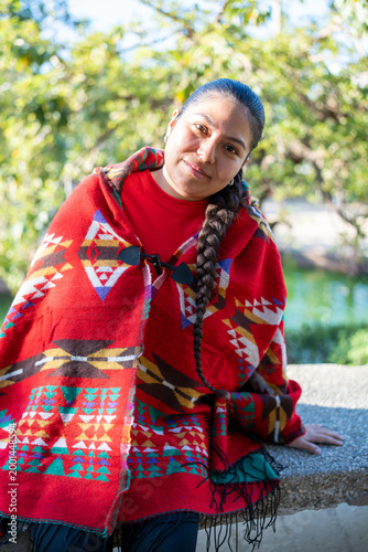 Indigenous Peruvian woman standing outdoors wearing a traditional red poncho