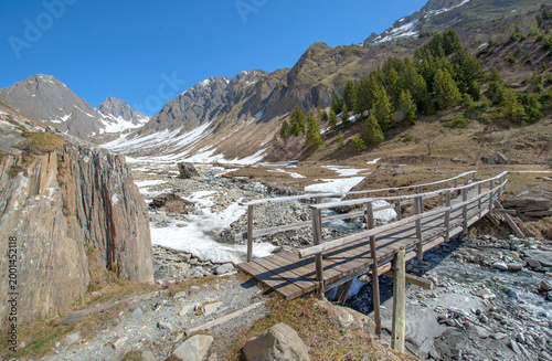 wooden bridge crossing  a stream flowing in  in rocky valley in french alps a...