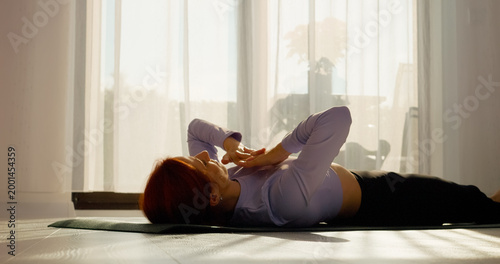 Fotografie In a bright living room, a woman engages in stretching and pilates exercises on a mat