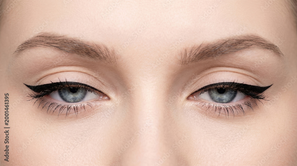 Fototapeta premium Extreme close-up of blue woman eyes with sharp black winged eyeliner makeup.