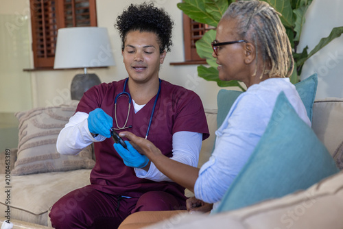 Fotografie Gloved male nurse on sofa checking senior African American woman's fingertip wit