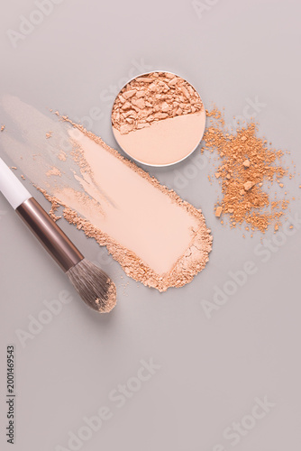 Beautiful vertical cosmetic background with samples of powder strokes in different tones, a refill of powder and makeup brush. Top view. copy space.