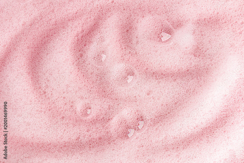 Obraz premium Delicate fluffy soap waves of foam with transparent bubbles on a pink background. A model of a cosmetic product for body skin care. detergent product.