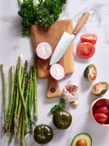 Fresh vegetables and herbs on marble countertop, prep tools