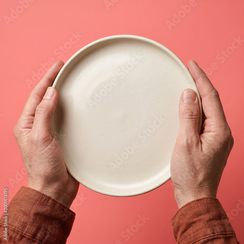 A person holding a white plate with both hands against a pink background.
