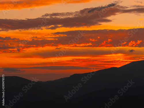 A stunning sunset paints the sky with vibrant oranges and reds, casting shadows over the majestic mountains in a serene landscape. Nature's beauty captivates the viewer.