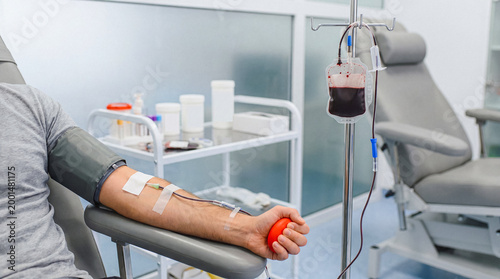 Canvastavla Man donating blood, with a full blood bag hanging from an IV stand, in a sterile medical clinic environment