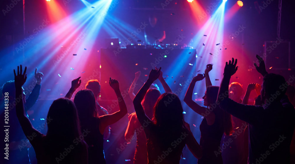 Obraz premium Silhouettes of energetic people dancing at a vibrant nightclub party with dazzling red and blue stage lights.